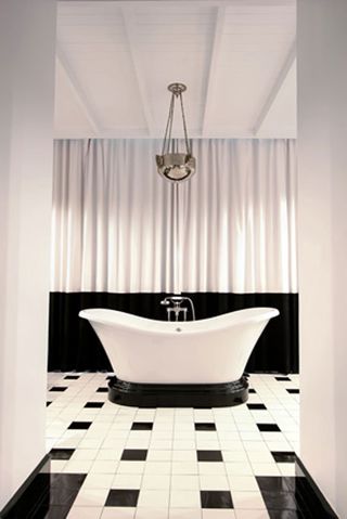 Free-standing bath on a black plinth, with white and black floor tiles and a black and white curtain