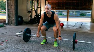 Man prepares to deadlift barbell from the floor in front of his garage