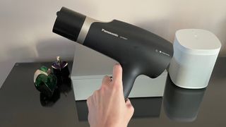The Panasonic EH-NA67 with the quick dry nozzle attached being held in a hand above a dressing table