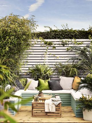 small decked garden with banquette seating painted in green and white fence behind