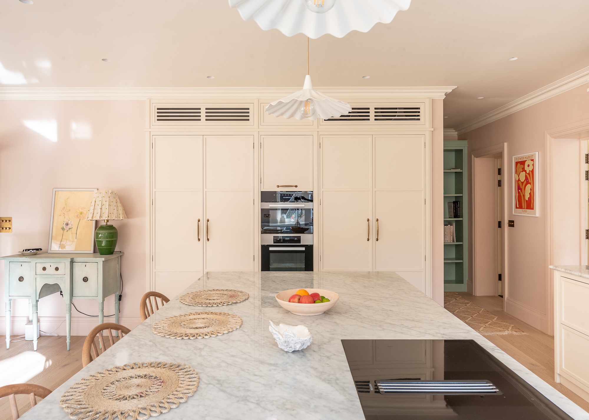 A creamish/pink colored kitchen with a large kitchen island in the middle as well as a stove and bar stools beside it