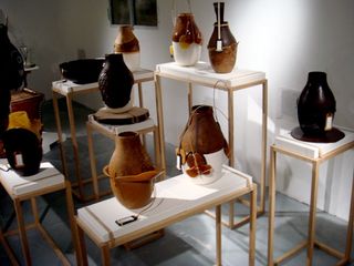 Nine ceramic vases on display. They vary in colour between brown, black and white.