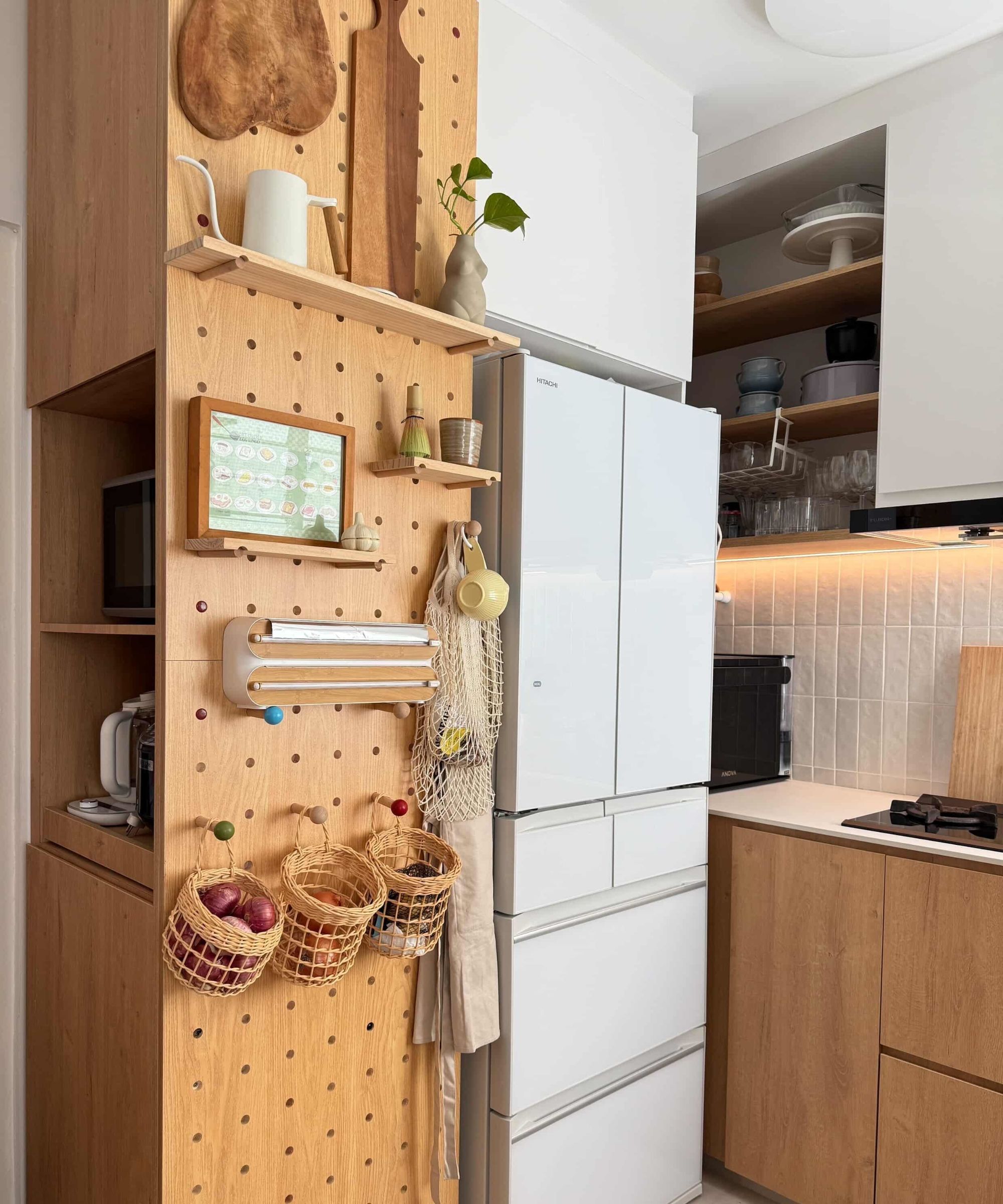 A small kitchen with wood and white cabinets, and a floor-to-ceiling pegboard housing shelving, hooks, and food baskets