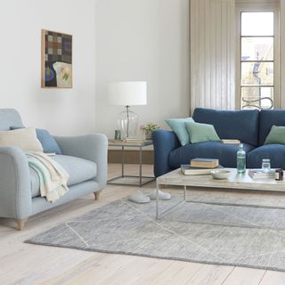 Navy blue sofa next to light blue armchair with glass coffee table
