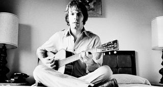 Bob Weir sits cross-legged on hotel room bed and strums his Martin acoustic