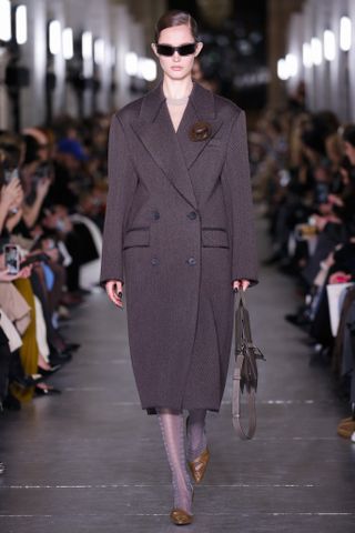 Tory Burch model wearing an oversize coat with a brooch attached to the lapel.