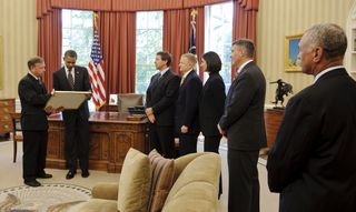 Space shuttle STS-133 mission Commander Steven Lindsey (far left) presents a montage to President Barack Obama in the Oval Office of the White House, as crew members Michael Barratt, Pilot Eric Boe, Nicole Slott, and Stephen Bowen along with NASA Administ