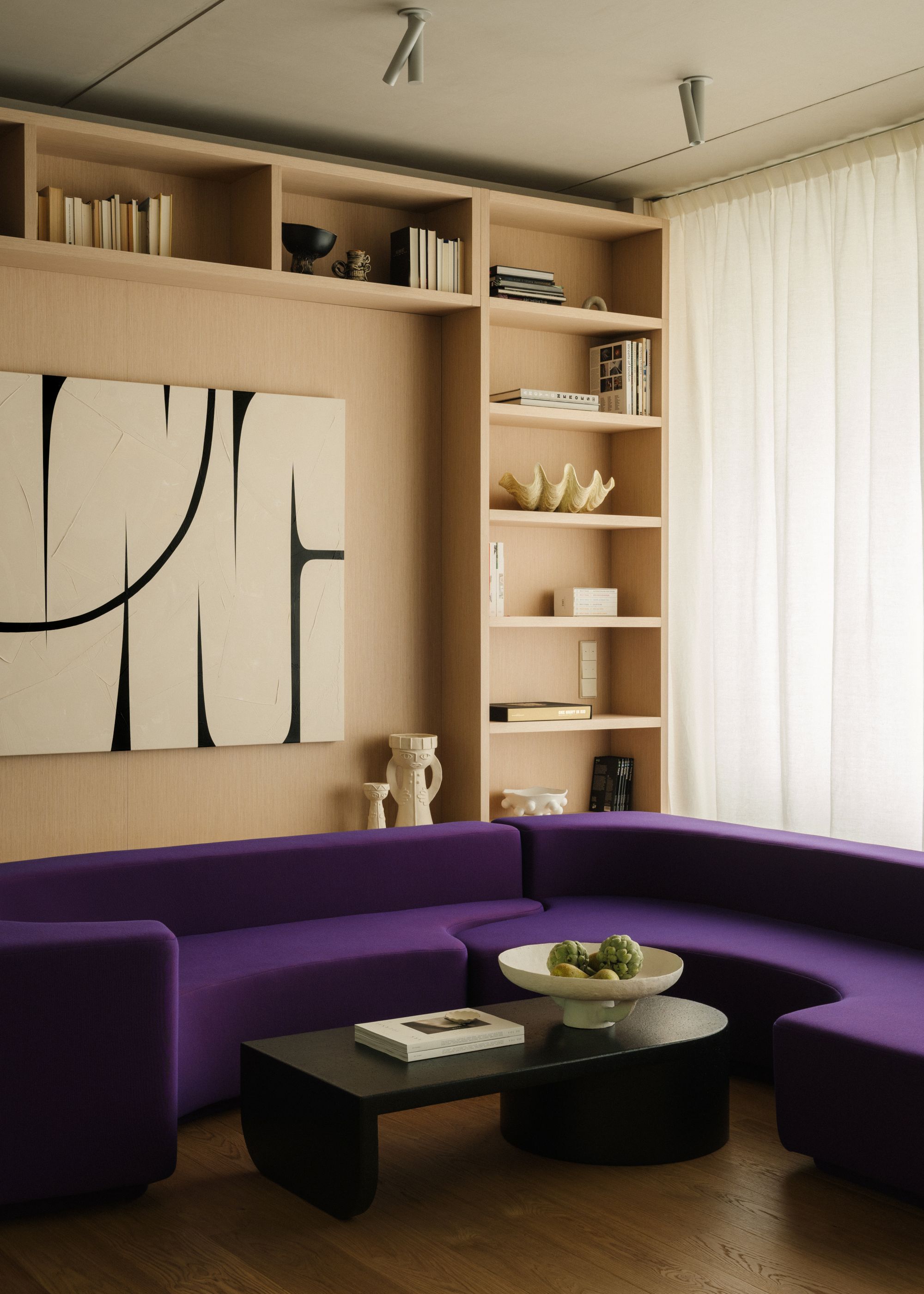 living room with a large purple couch in front of a built in shelving unit in light wood