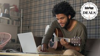 A man uses a laptop while playing acoustic guitar