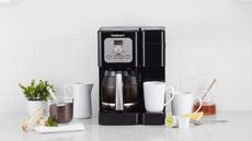 How to clean a Cuisinart coffee maker: Cuisinart's drip coffee maker on a white countertop with a carafe of coffee and mugs around it