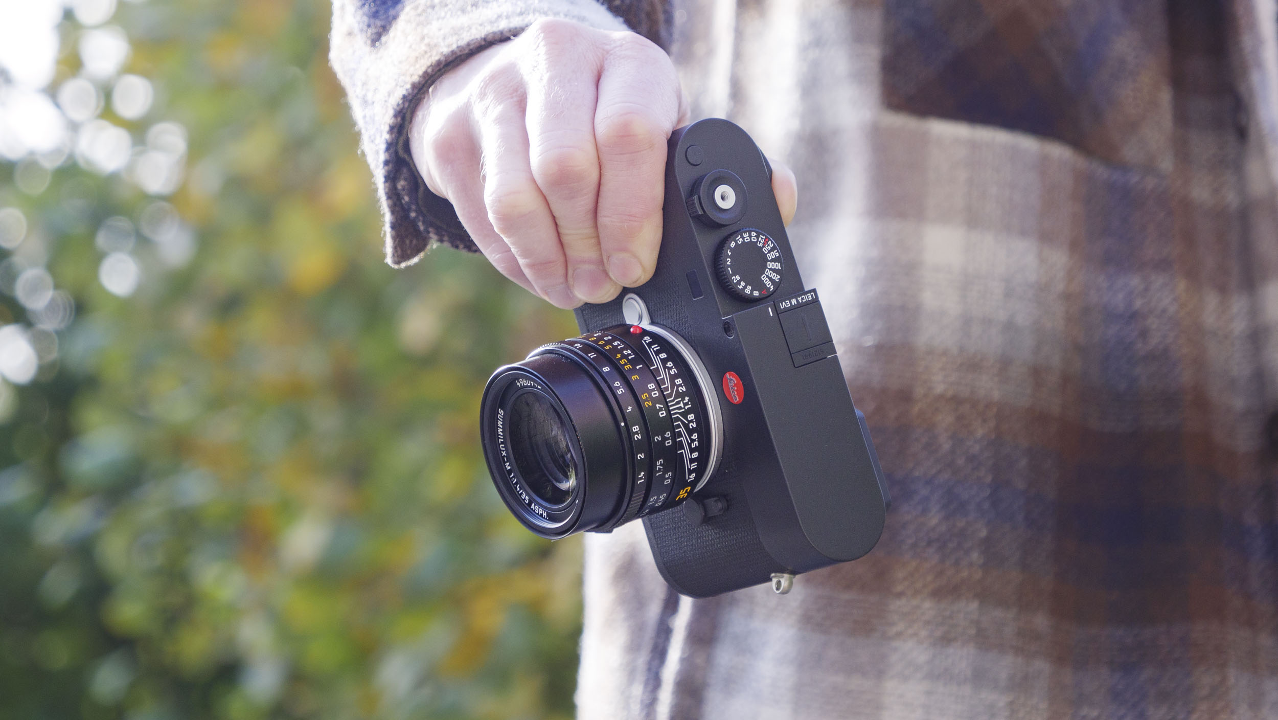 Leica M EV1 camera in user&#039;s hands, autumn leaf backdrop