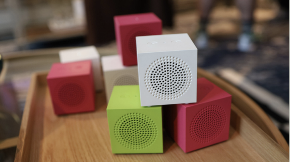 Several IKEA Kallsup speakers in pink, green and white on a wooden table, with TR's CES badge in the top right corner