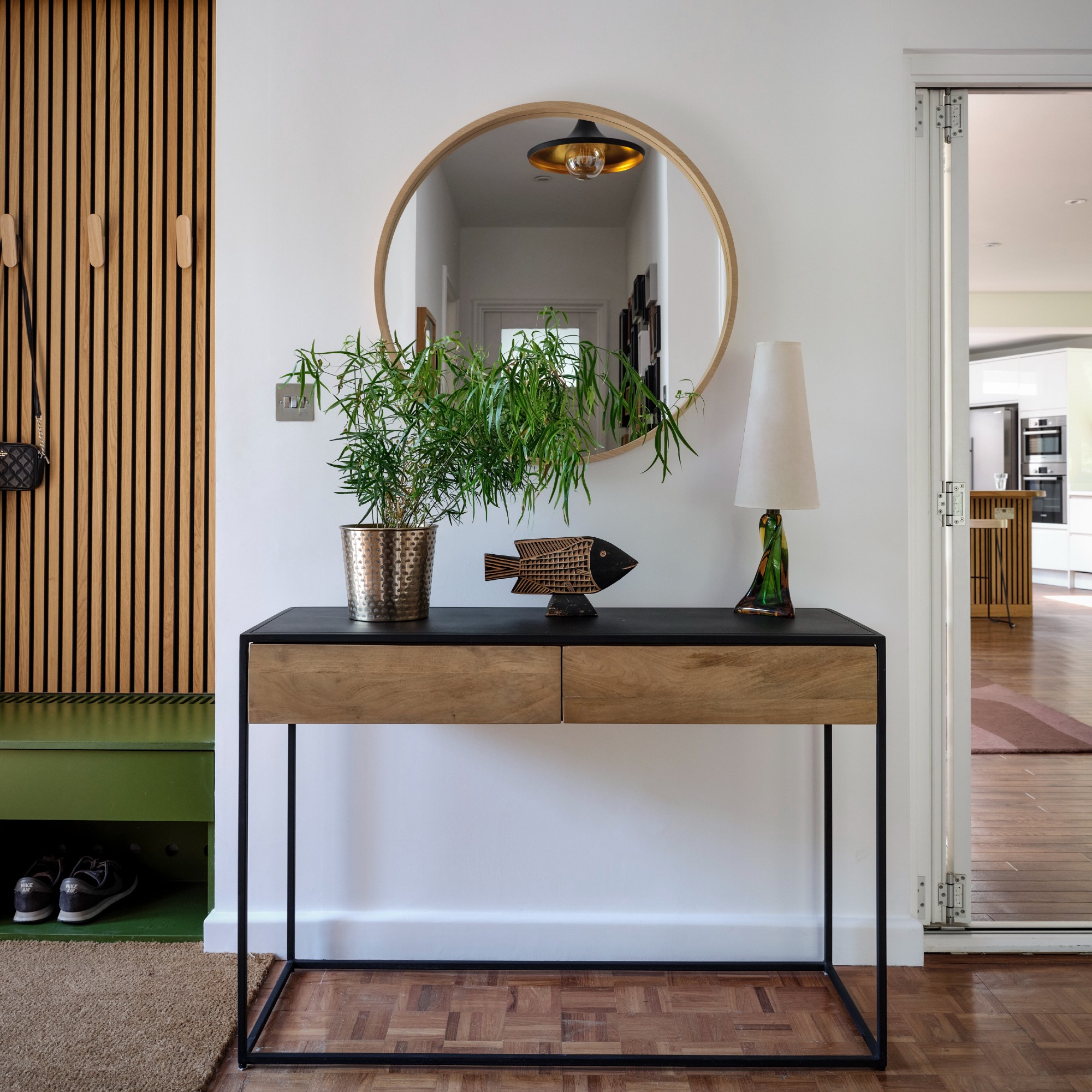 A white hallway with a console table and a round mirror hung above it reflecting a narrow entryway