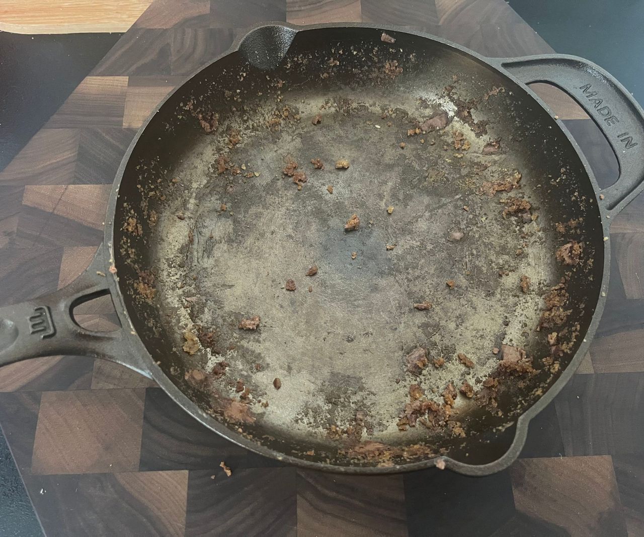 A small bronze colored cast-iron skillet with cookie crumbs inside.