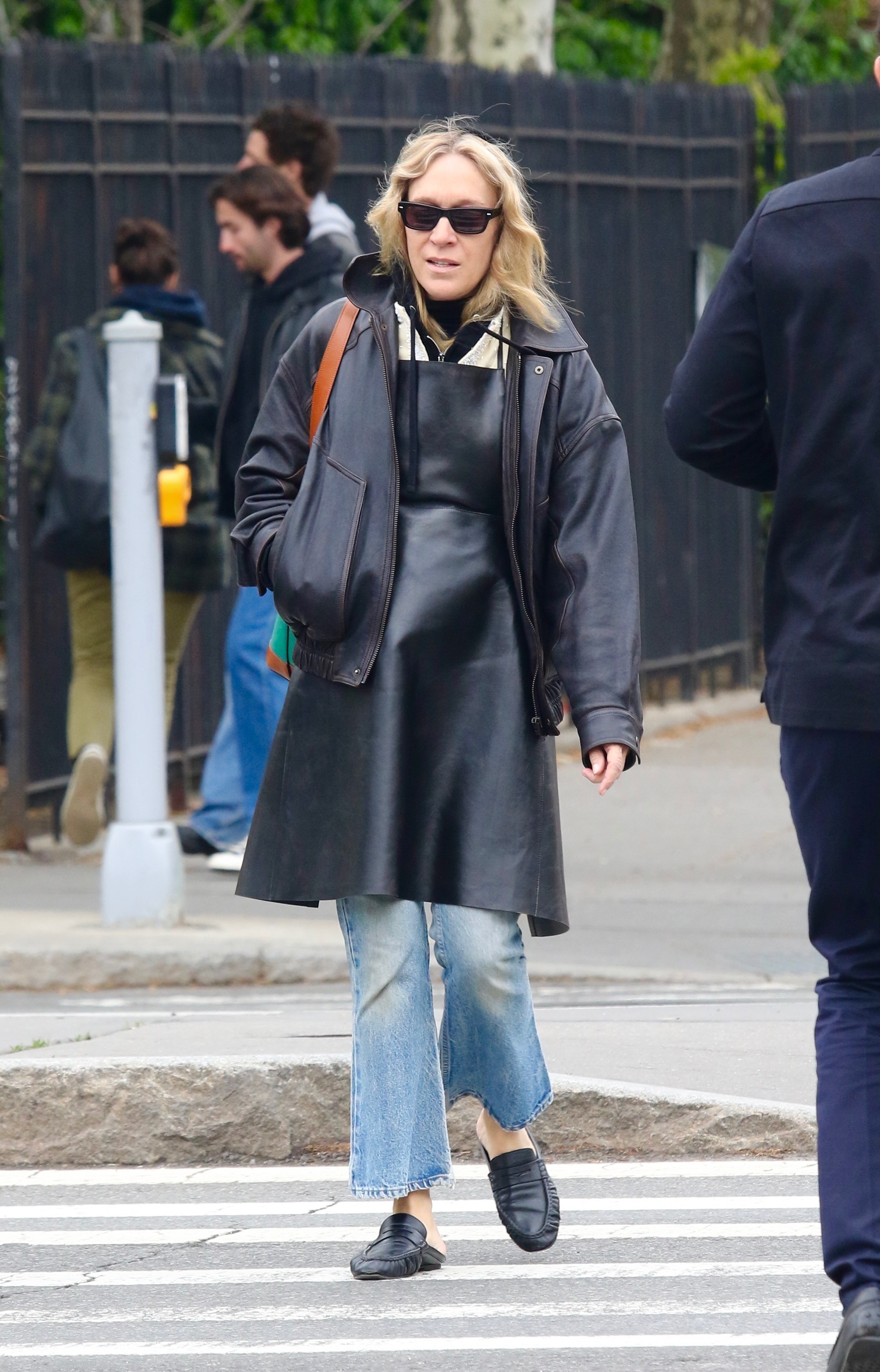 Chloe Sevigny walks down the street in New York wearing a leather apron with jeans and backless loafers.