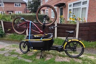 The Raleigh Stride 2 e-Cargo bike has another bike mounted upside down on it's cargo tub in a front garden.