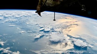 Components of a space station are seen in silhouette against the blue and white horizon of Earth below.