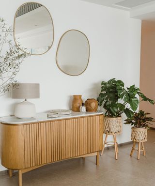 Entryway with sculptural round mirrors, wooden console, decorated with table lamps and plants