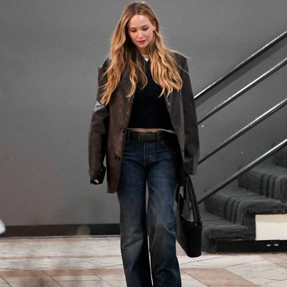 Jennifer Lawrence wearing blue jeans with a brown leather blazer, a black top, and a black handbag