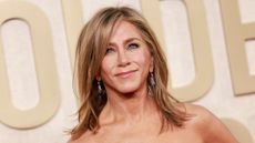 Jennifer Aniston smiling with a mousey blonde side-part long bob and wearing a strapless black gown