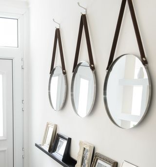 Three round mirrors with leather straps hanging on white wall behind white front door