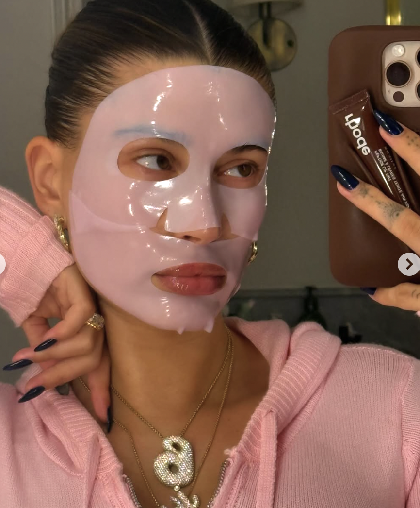 Hailey Bieber in a pink sheet bask, pink sweater, with navy nails