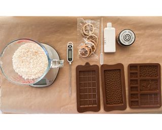 Equipment required to make wax melts including soy wax, silicone molds, gilded metal flakes, thermometer and dried orange slices