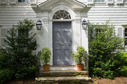 How to paint a front door – House with white siding and blue gray front door with foliage plants either side
