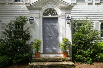 House with white siding and blue gray front door with foliage plants either side