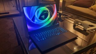 The Razer Blade 16 at CES 2025, on a glass table and with its keyboard lit up in blue.