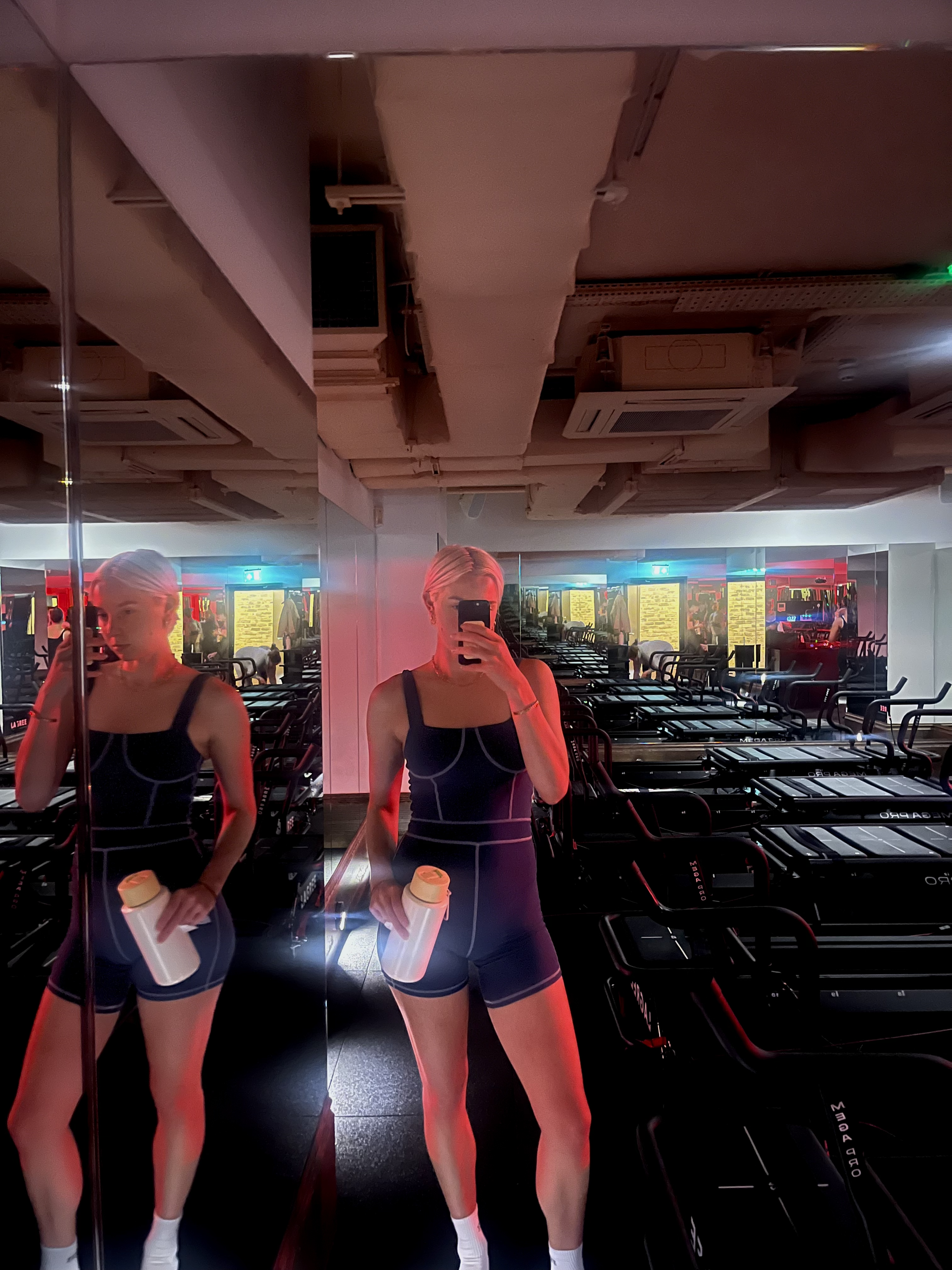 A woman takes a mirror selfie in a Lagree fitness studio