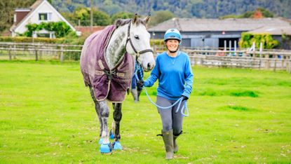 Woman bringing rugged up grey horse in from the field