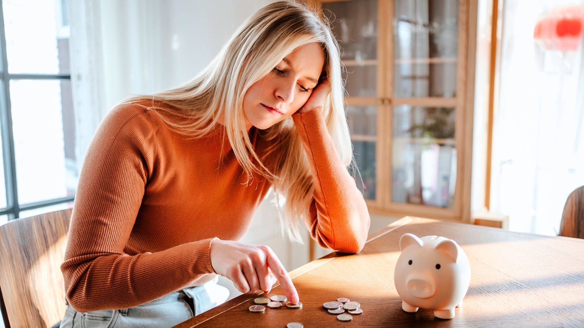 Woman contemplating savings with piggy bank and coins at home