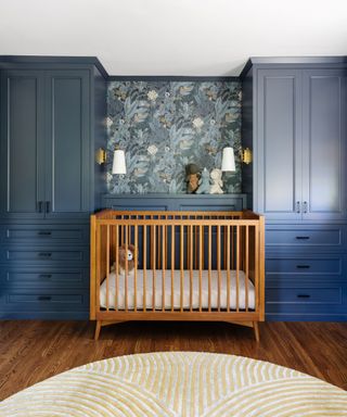 nursery with dark blue walls and wooden cot in alcove with blue patterned wallpaper