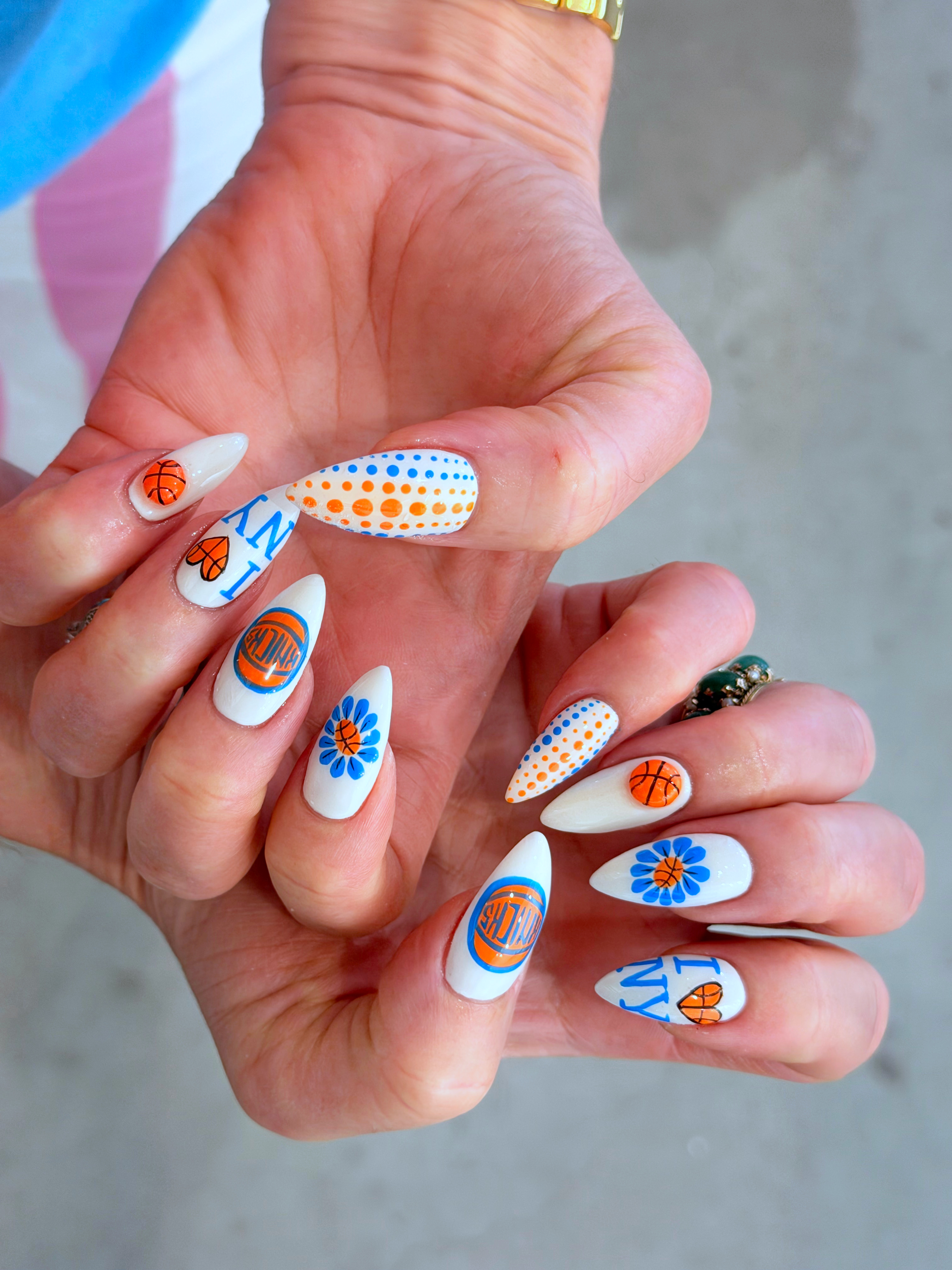 a white manicure with almond shape and blue flower and New York Knicks designs
