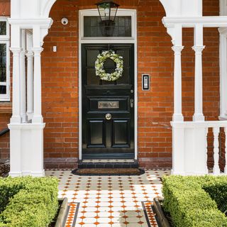 Front of brick house with black door and red and white tiled path