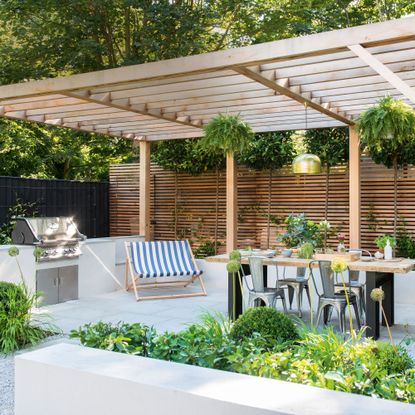Outdoor kitchen with wooden pergola, striped sunchair and wooden dining table