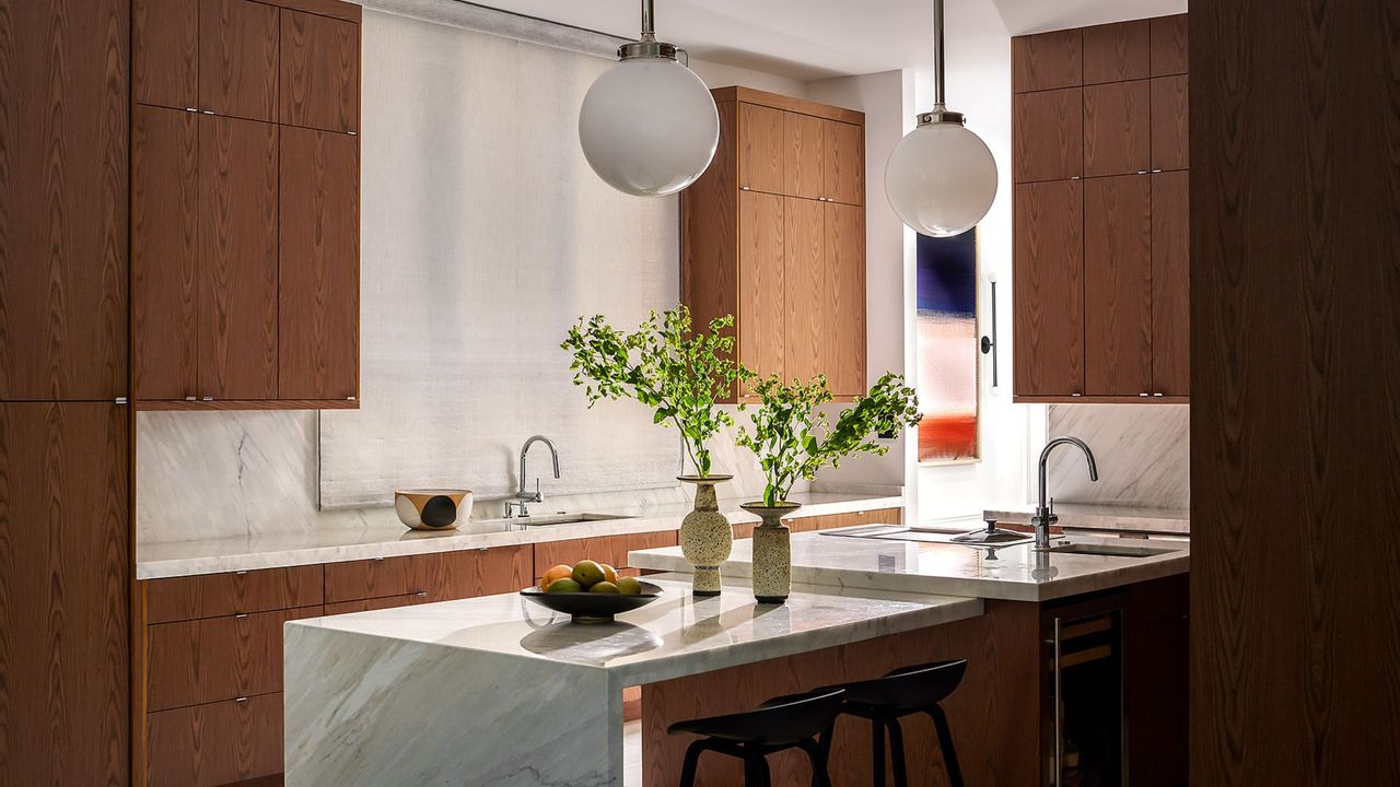 A kitchen with wooden cabinets, pendant lights and a marble island
