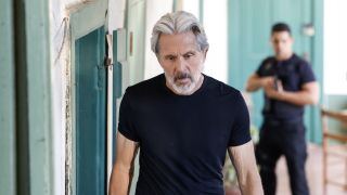 Gary Cole's Alden Parker on black t-shirt with Nick Torres standing behind him with gun drawn