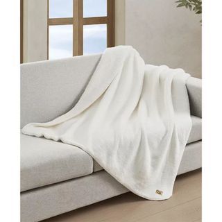 A large white super soft throw blanket draped over the end of a modern grey sofa