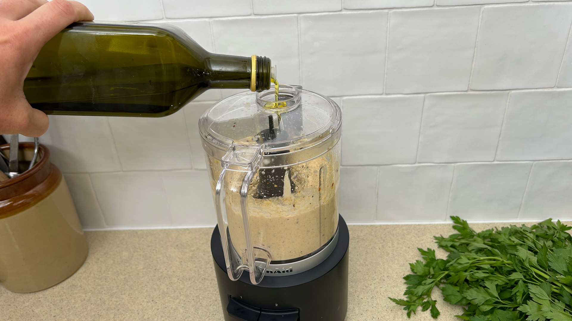 Pouring olive oil into hummus made in the KitchenAid Go Cordless Food Chopper