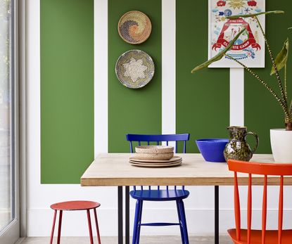 A dining area with a wooden table, colorful chairs, and green color blocked patterns on the walls