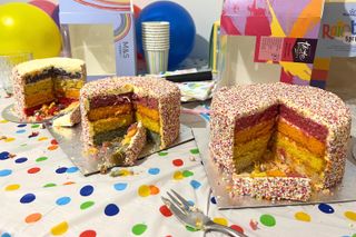 Three rainbow cakes cut to reveal rainbow layers lined up on a table covered in party decorations