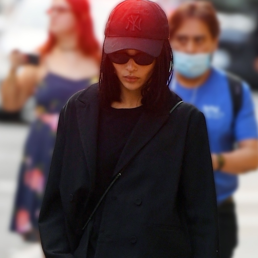 Zoe Kravitz walking in New York City wearing a black Yankees baseball cap, black oval sunglasses, a boxy black blazer, and a black crossbody bag