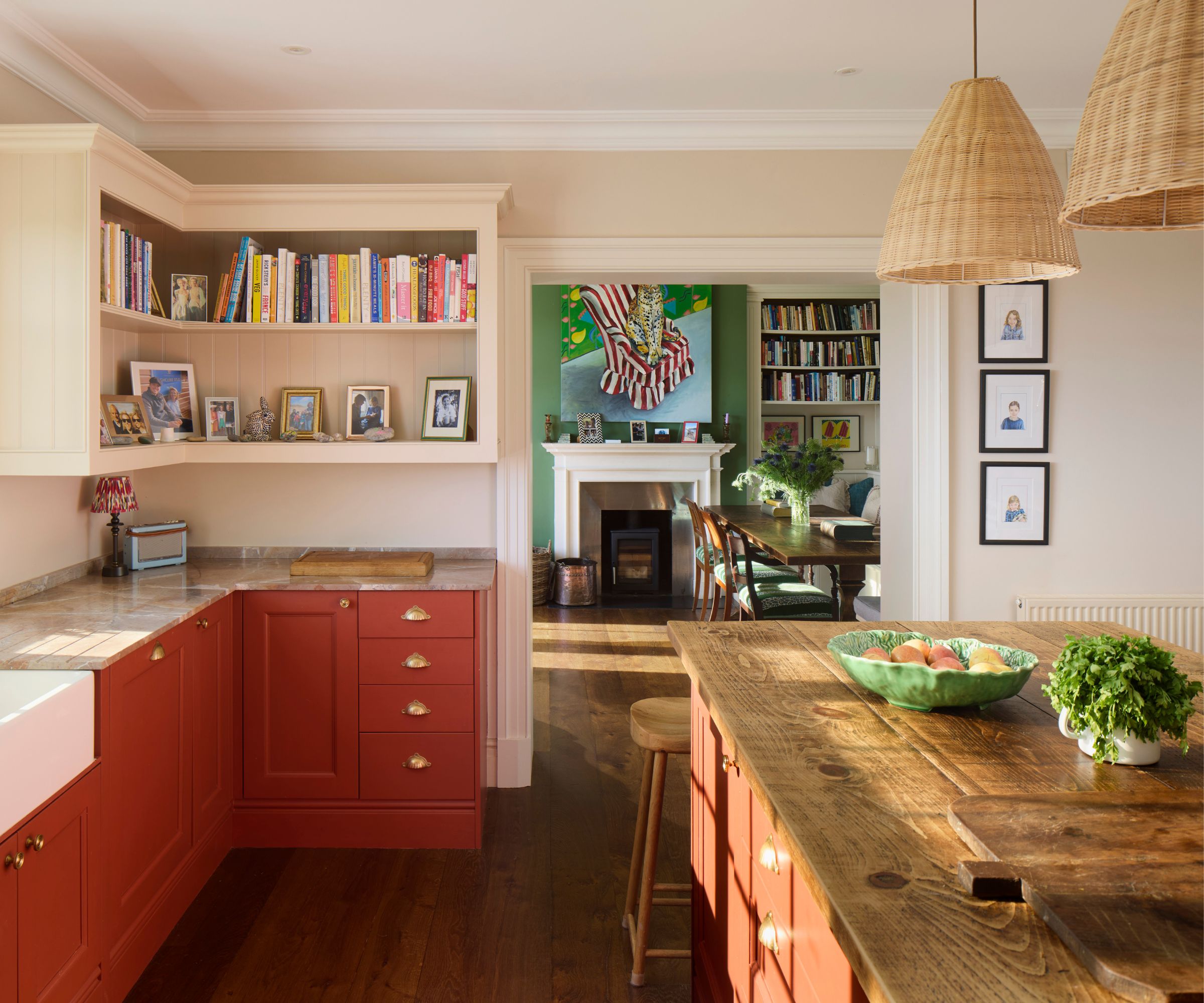 A soft kitchen with dark red cabinets, open shelving, rattan pendant lights, and a wooden countertop on the island