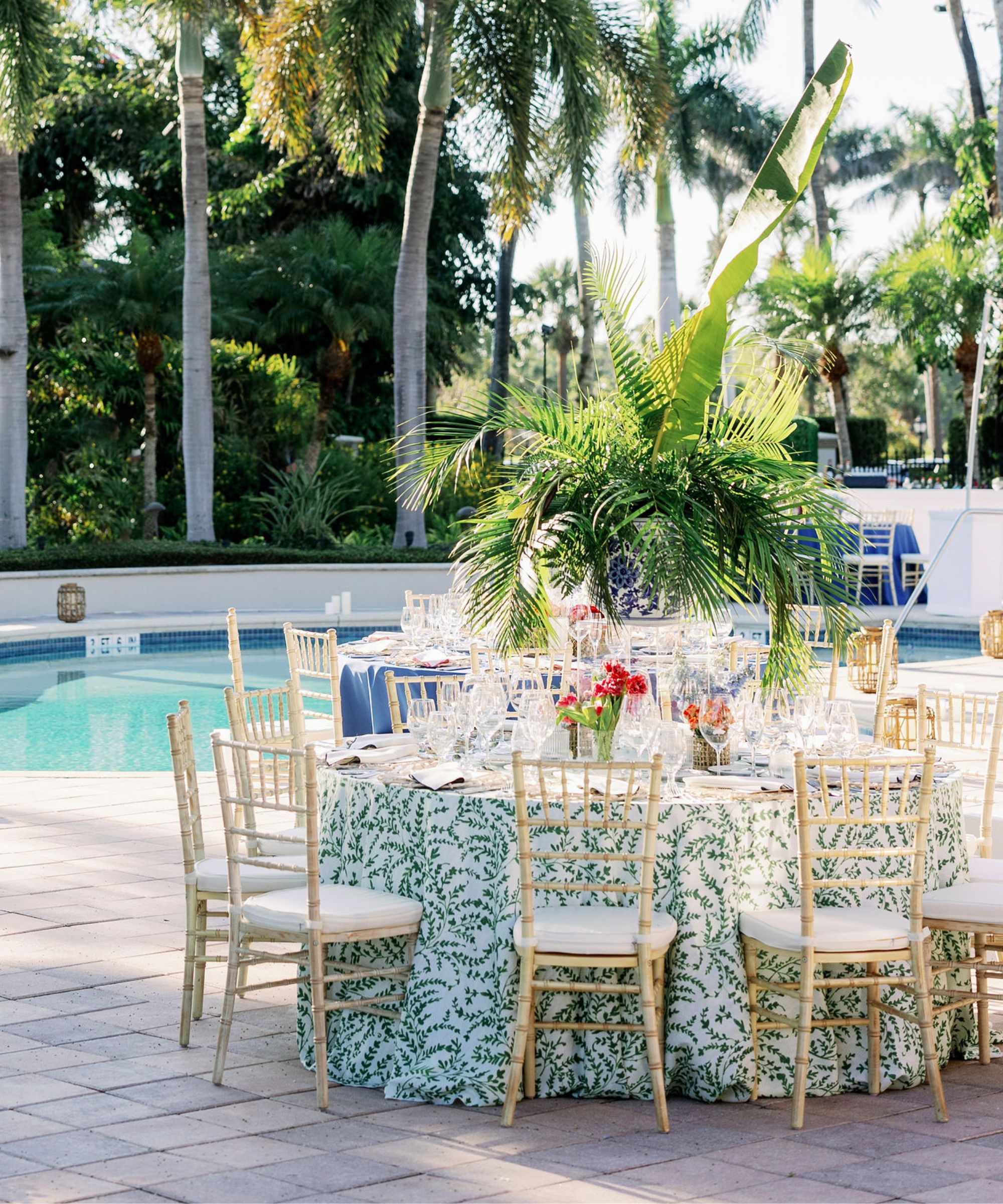 Tropical themed table set up by a pool with palm trees in the background