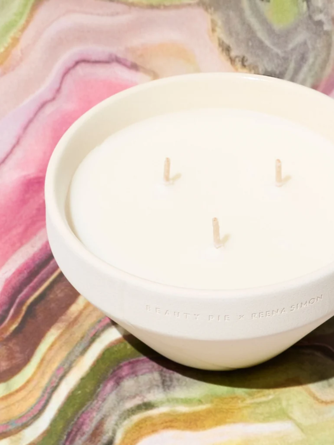 A ceramic three-wick candle from Reena Simon x Beauty Pie on a marbled surface