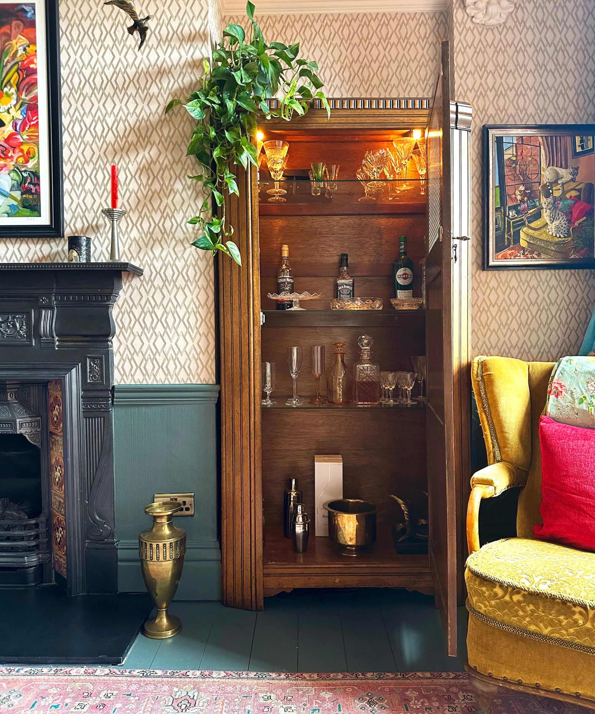 Living room with fireplace, printed wallpaper, yellow armchair and wood bar cabinet with glassware