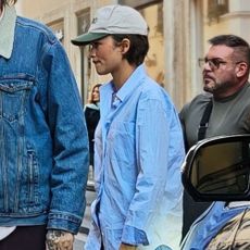 Zendaya walks down the street wearing a blue button down shirt with black leather loafers and blue jeans.