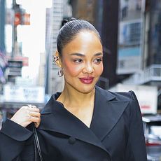 Tessa Thompson wearing a black cinch waist blazer, big black pants, and black pointed-toe punps with a silver applique